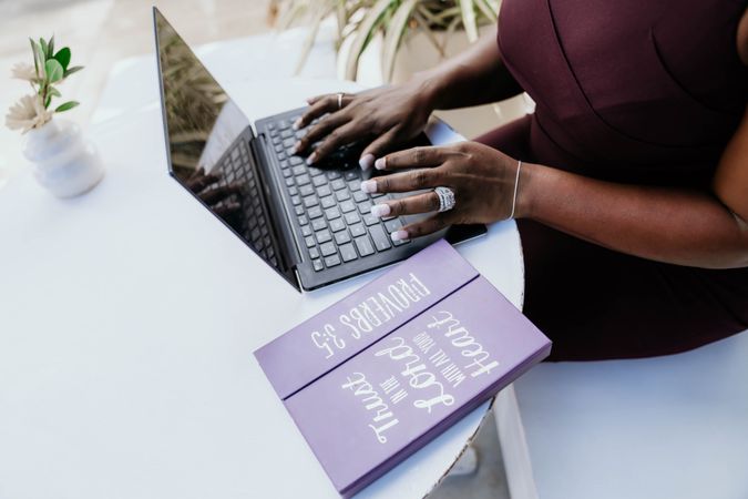 Cropped image of Black woman in purple dress working on her laptop