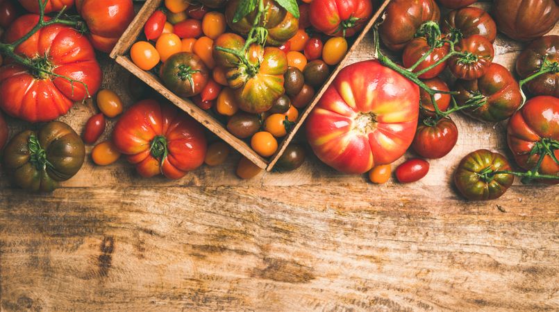 Assortment of different tomatoes in square box, on wooden table, with copy space