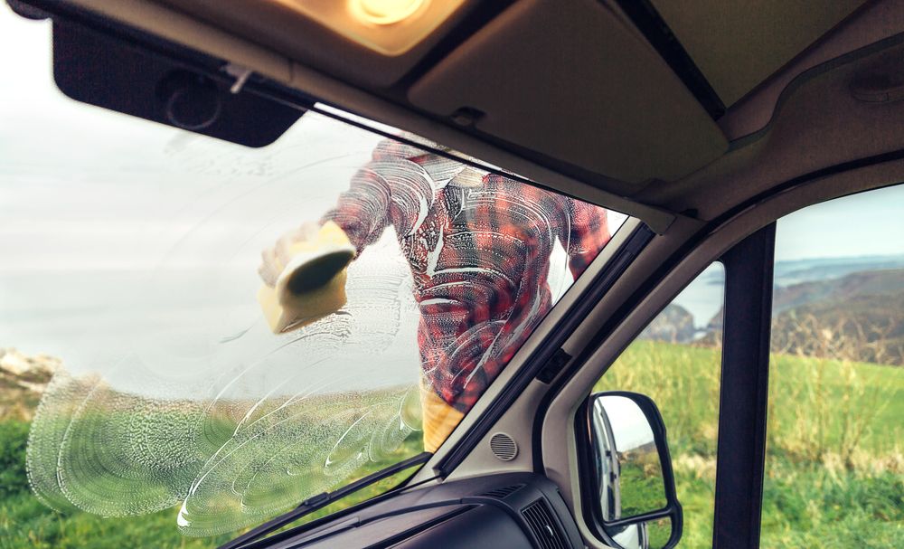 View from inside van of man in checkered red shirt cleaning front window