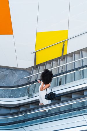 Pregnant Black woman browsing smartphone on escalator