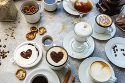 Coffee drinks with foam art on table with cinnamon sticks, dried orange and coffee beans