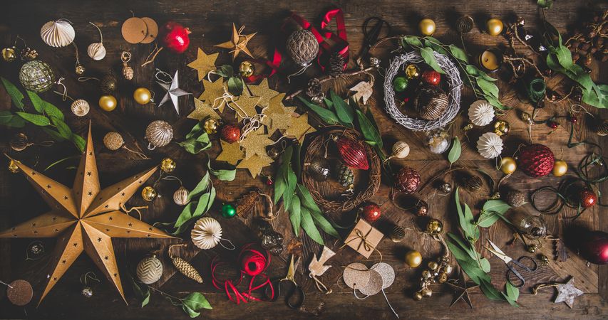 Holiday decorations of stars, baubles, leaves, scissors and ribbon strewn on wooden table