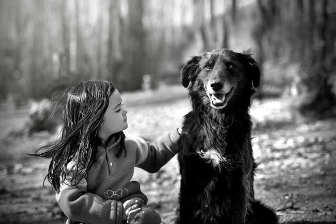 Grayscale photo of girl sitting beside dog outdoor