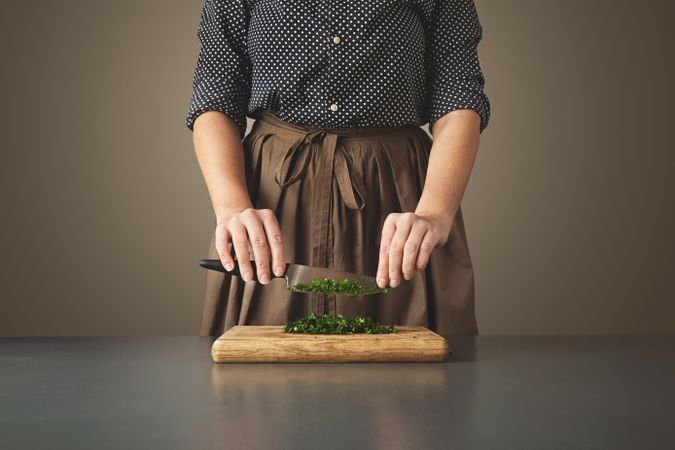 Woman holds knife above parsley she’s chopping