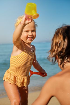 Charming girl in yellow swimsuit having fun with watering can