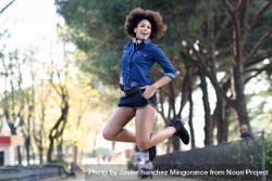 Female jumping with knees back in denim shirt with open arms in front of trees 0V36G5
