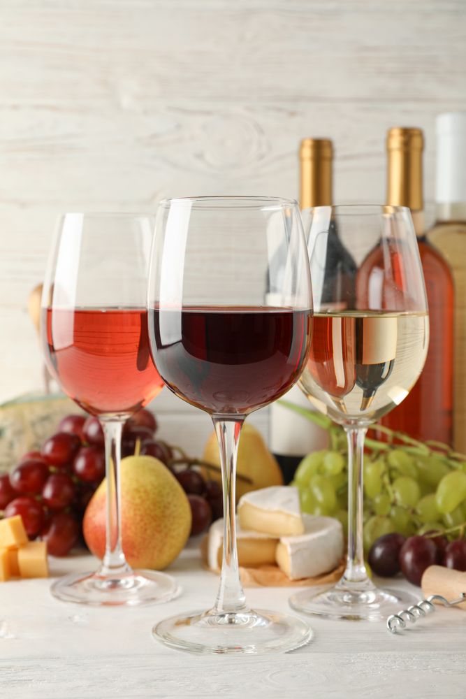 Fruits, cheese, bottles and glasses with different wine on light background, space for text