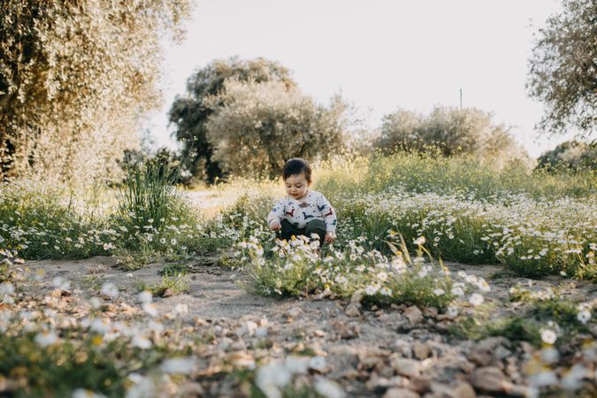 Young boy crouching to play with daisies