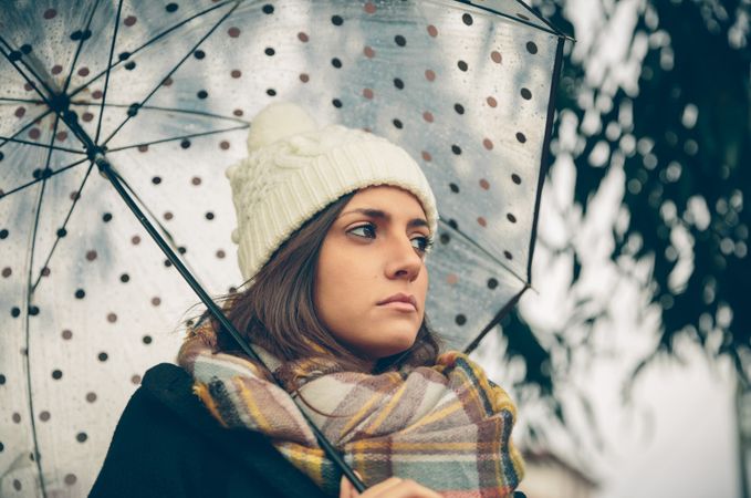 Woman standing under umbrella deep in thought