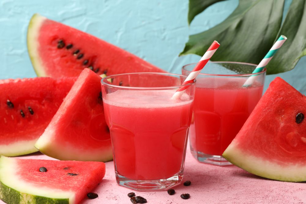 Composition with glass of watermelon juice and slices on pink table