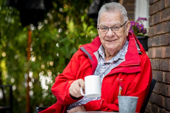 Older man wearing red jacket sitting with coffee mug