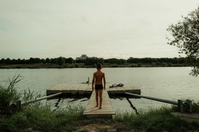 Child in swimming trunks walking along pier to water