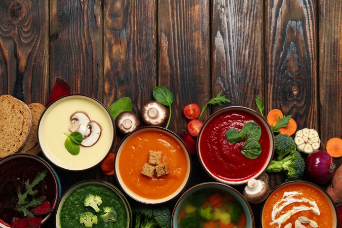 Top view of colorful soups lined up on bottom of dark wooden table with copy space