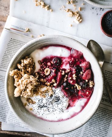 Delicious breakfast bowl with quinoa, rice and groats near tea cup and newspaper