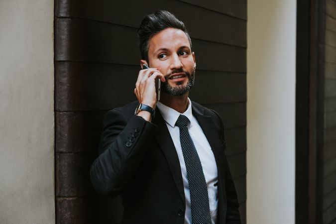 Adult stylish man in costume talking on smartphone near wall