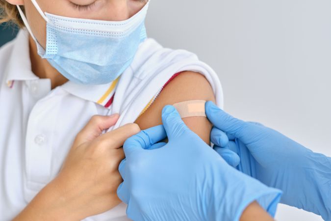 Crop doctor applying patch on shoulder of patient in mask