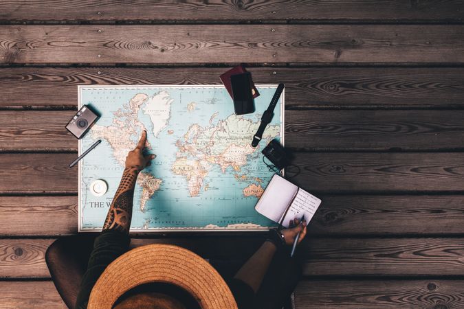 Top view of woman making her vacation plan sitting in front of world map