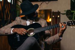 Stylish Black man in classic outfit playing guitar
