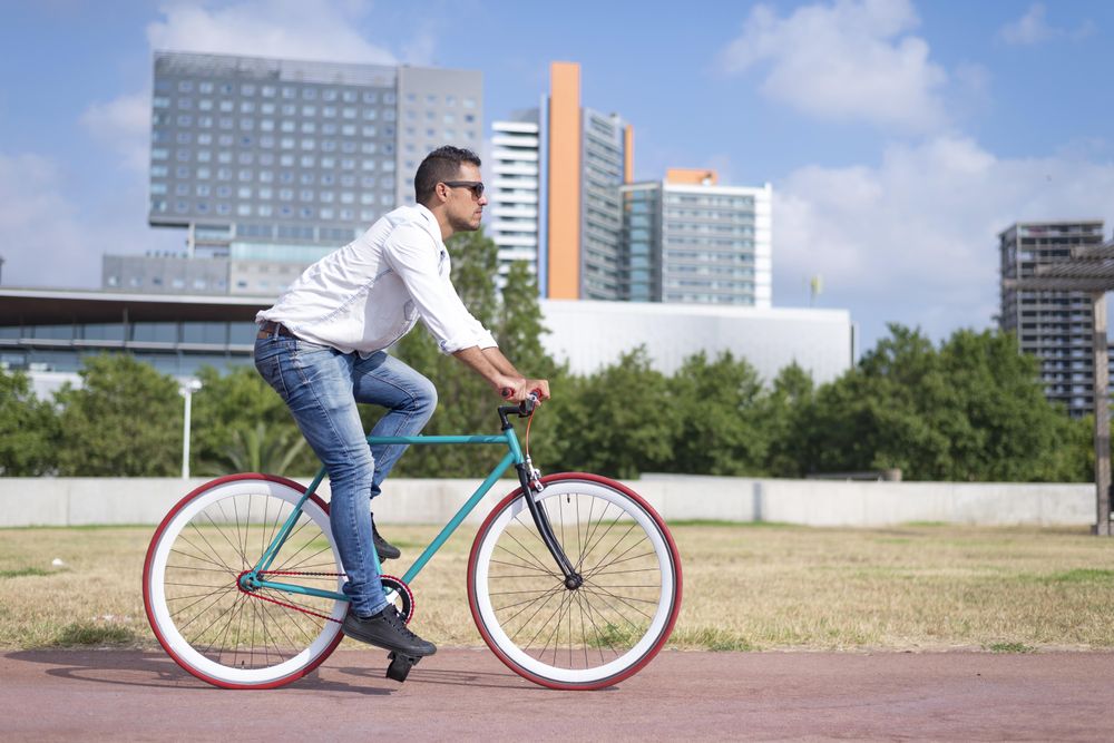 Male riding red and green bike outside next to city buildings on sunny day