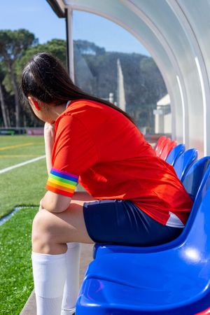Female soccer player with LGBT pride captain armband on the field bench