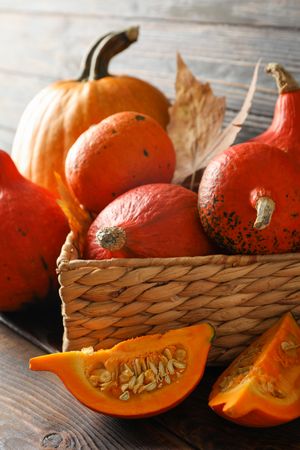 Pumpkins in straw basket on wooden background, close up