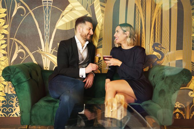 Couple enjoying cocktails on green sofa in bar