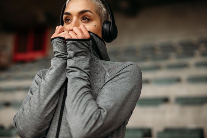 Fitness woman relaxing after workout listening to music on headphones standing in a stadium
