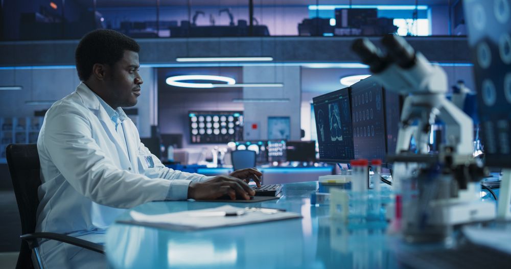 Black Male Neuroscientist Using Desktop Computer To Analyze MRI Scans Of Brain In Medical Research Center Laboratory.