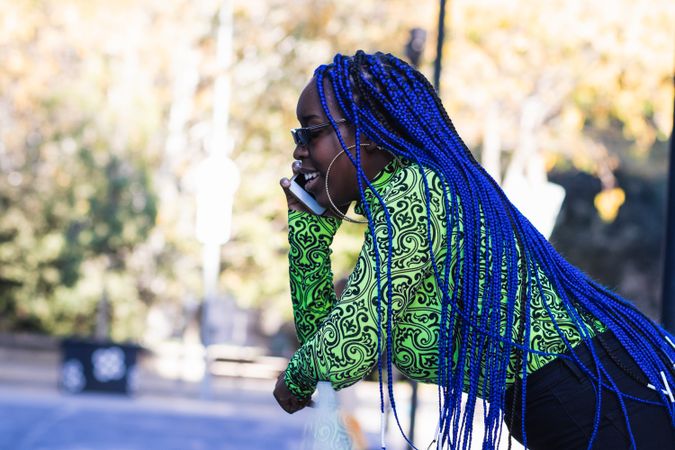 Cheerful Black woman with blue hair speaking on smartphone