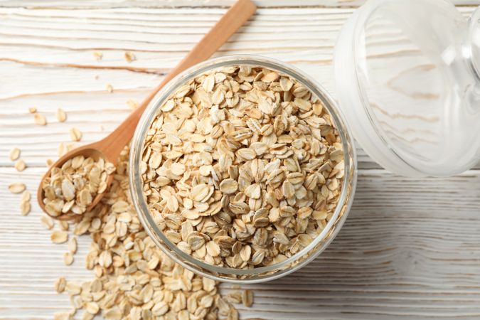 Glass jar with oatmeal and spoon on wooden background, top view