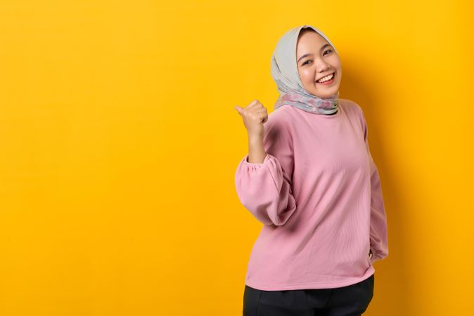Excited Muslim woman in head scarf pointing behind her