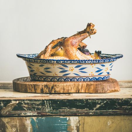Cooked chicken in ceramic dish displayed on rustic wood tray
