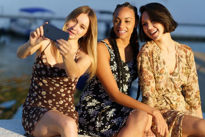 Three happy women sitting near coast taking selfie