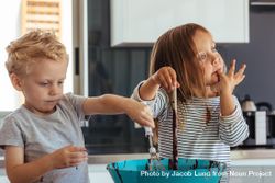 Little boy and girl mixing batter in a bowl for baking, with girl licking her fingers 0yzM75