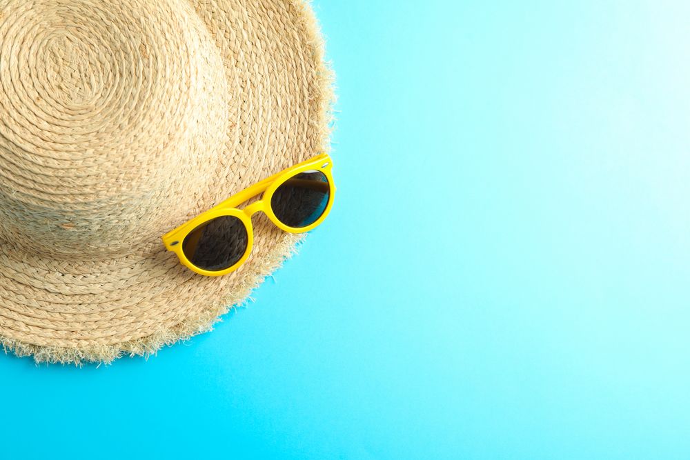 Straw hat and sunglasses on color background, space for text