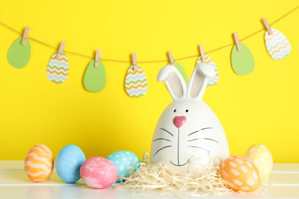 Decorated bunny and Easter eggs on table against color background