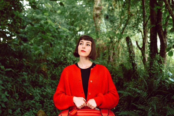 Woman in red with big red suitcase in forest