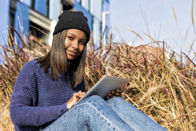 Female in hat sitting outside with tablet