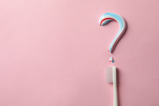Question mark made of toothpaste and toothbrush on pink background