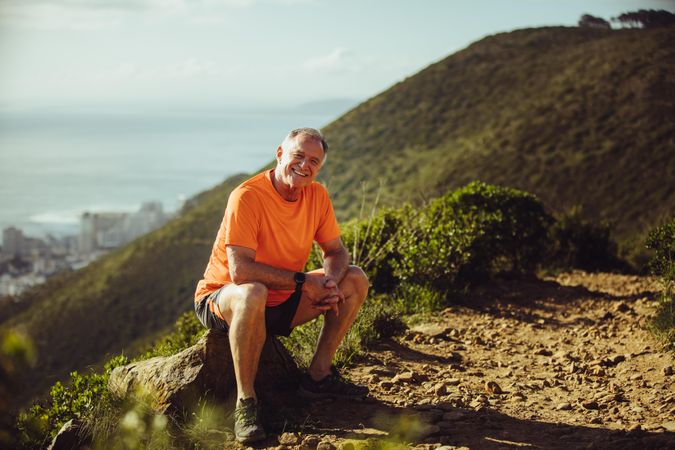 Athletic man sitting on a rock taking a break after trail running