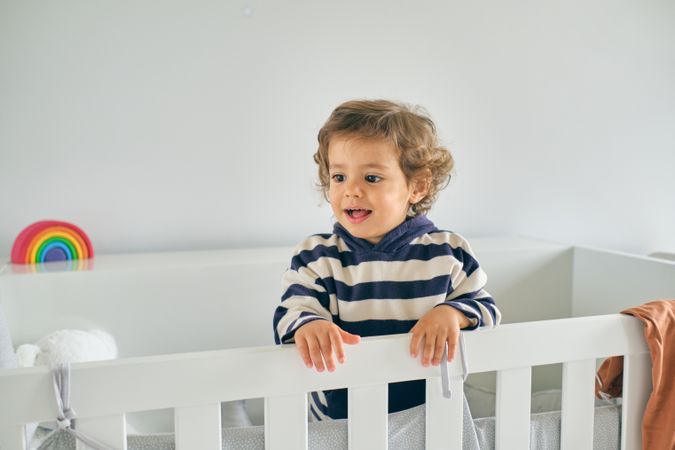 Positive little boy standing in crib