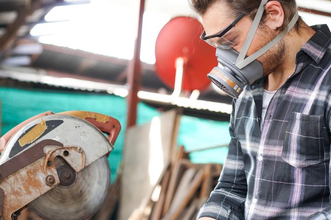Man in dust mask with saw in carpentry shop