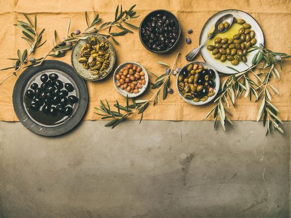 Olives in bowls with branches, on concrete with beige table linen