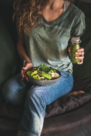 Woman in t-shirt and jeans sitting and holding vegetarian bowl