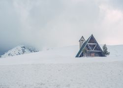 Wooden house with triangular roof located on snowy hill