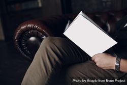 Side view of man sitting on brown couch reading a book 0yQ6n0