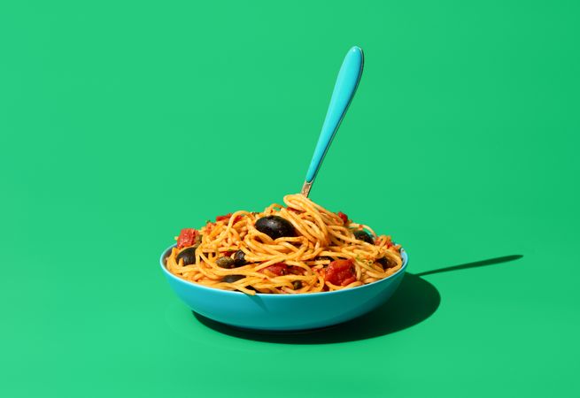 Pasta puttanesca dish, minimalist on a green background
