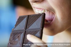 Girl biting into square of dark chocolate 4jVrLr