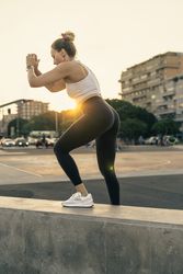 Athletic woman performing a step-up exercise during an outdoor urban workout at sunset
