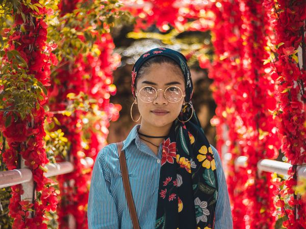 Woman wearing floral scarf on her head and standing in front of red flowers